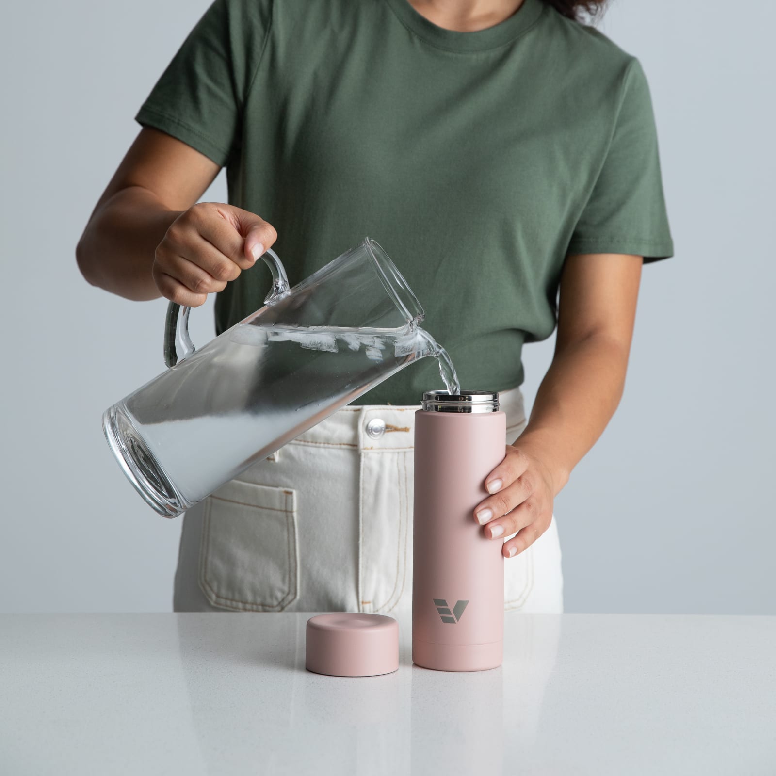 A female filling her Ever Vessel Multi Rose Pink stainless steel tea infuser water bottle with iced water at the kitchen bench.