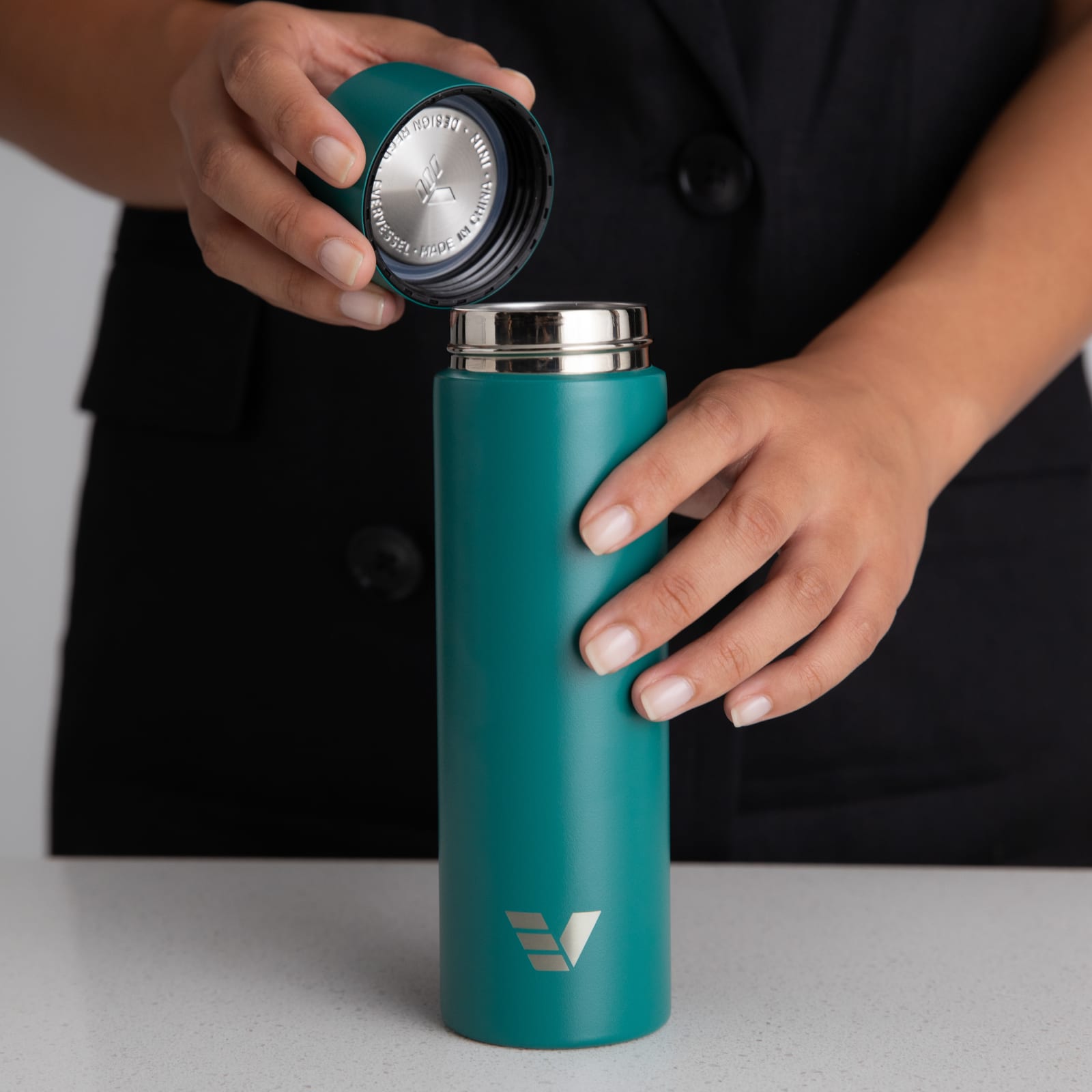 Female taking the lid off her Ever Vessel Mini Teal green small water bottle at a stone bench.