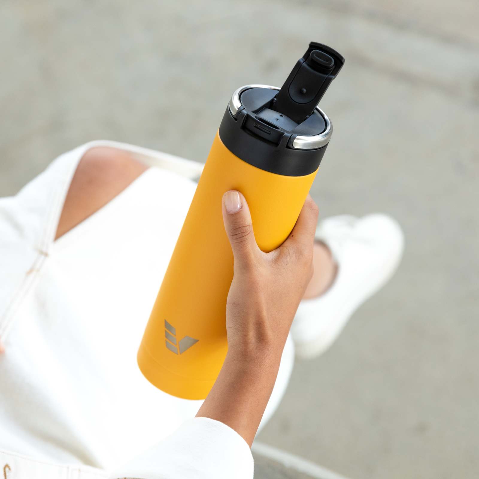 A female about to drink from her Ever Vessel Maxi Yellow stainless steel water bottle with the flip top lid open.