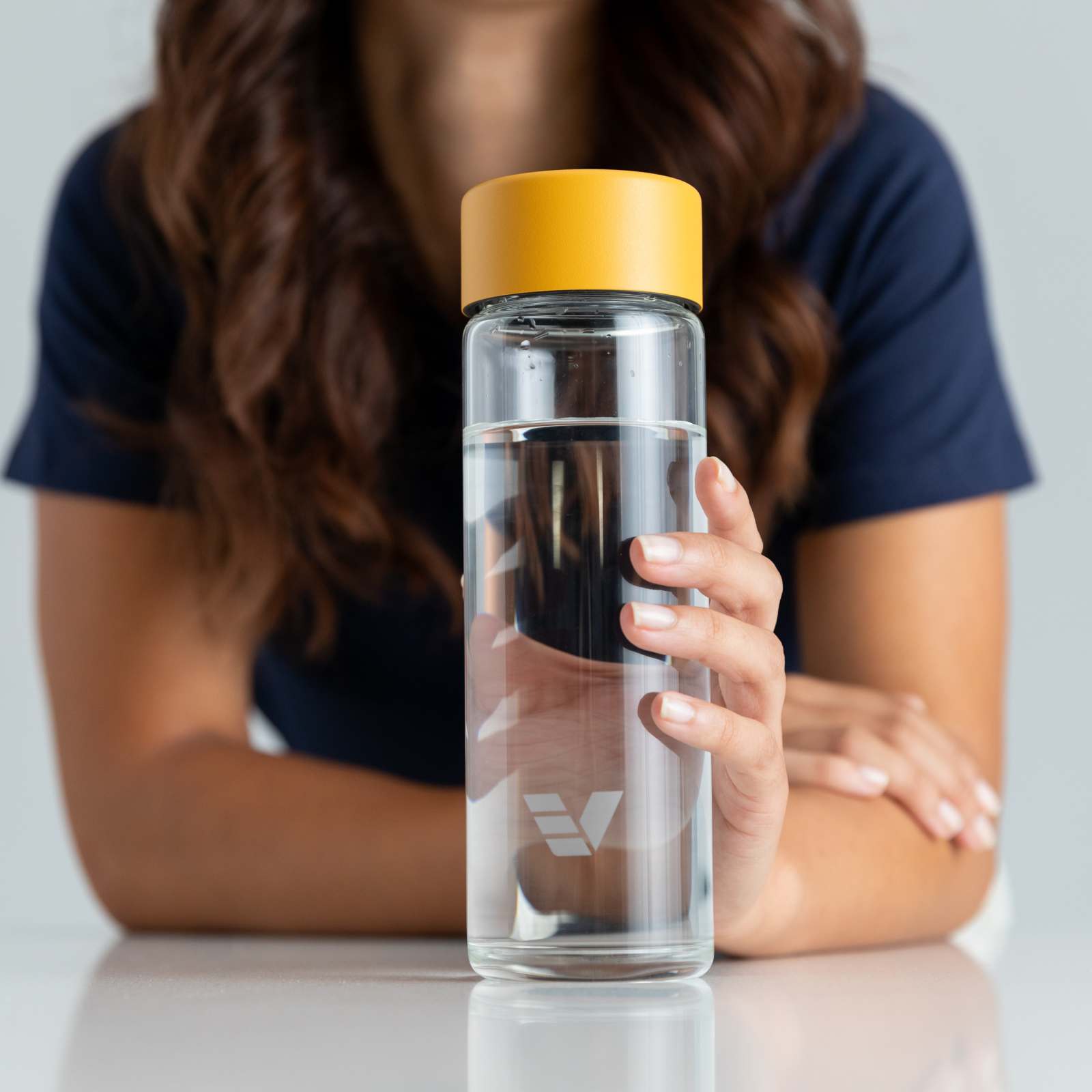 A female holding her Ever Vessel Glass water bottle with yellow lid on a kitchen bench.