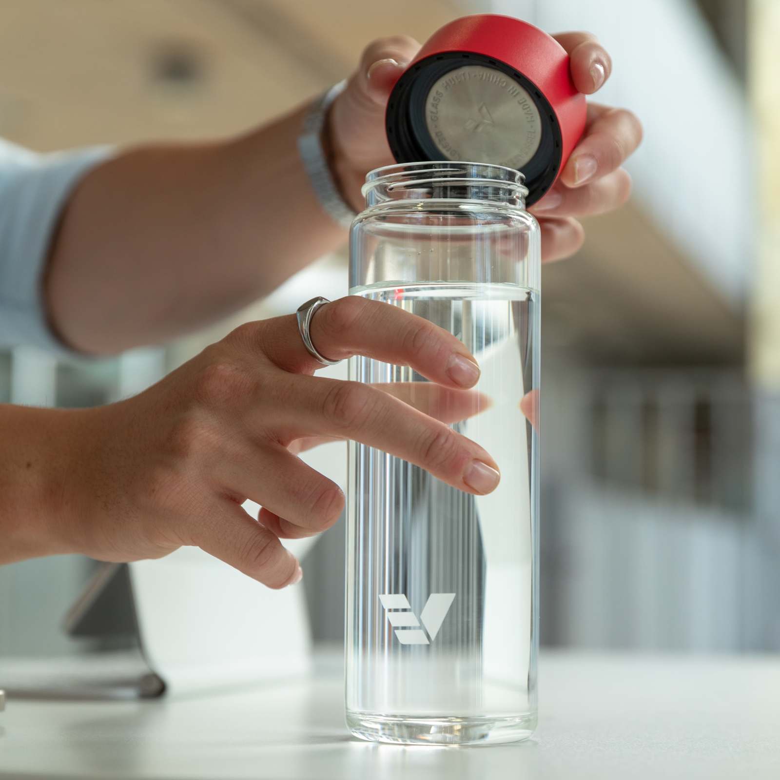 A male taking off the red lid from his Ever Vessel Glass water bottle at his work desk.