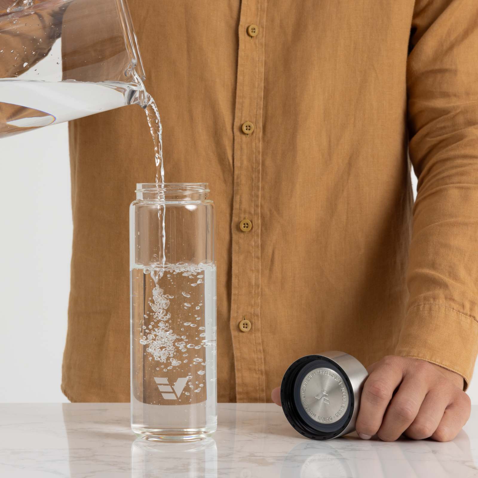 A male filling his Ever Vessel Glass water bottle with stainless steel lid at the kitchen bench.