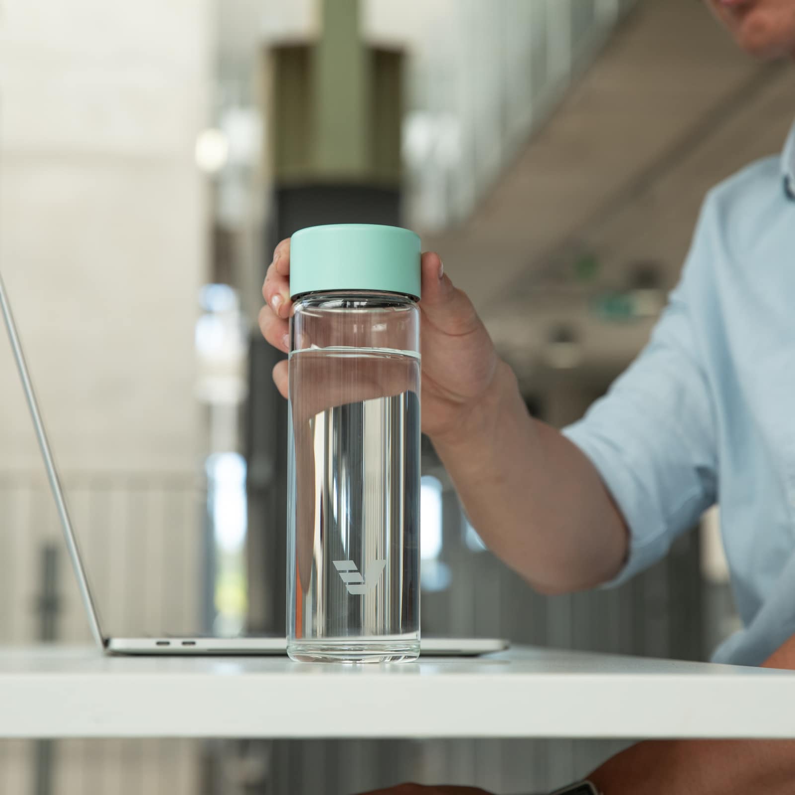 A male picking up his Ever Vessel Glass Multi tea infuser water bottle with a mint green lid off his desk.