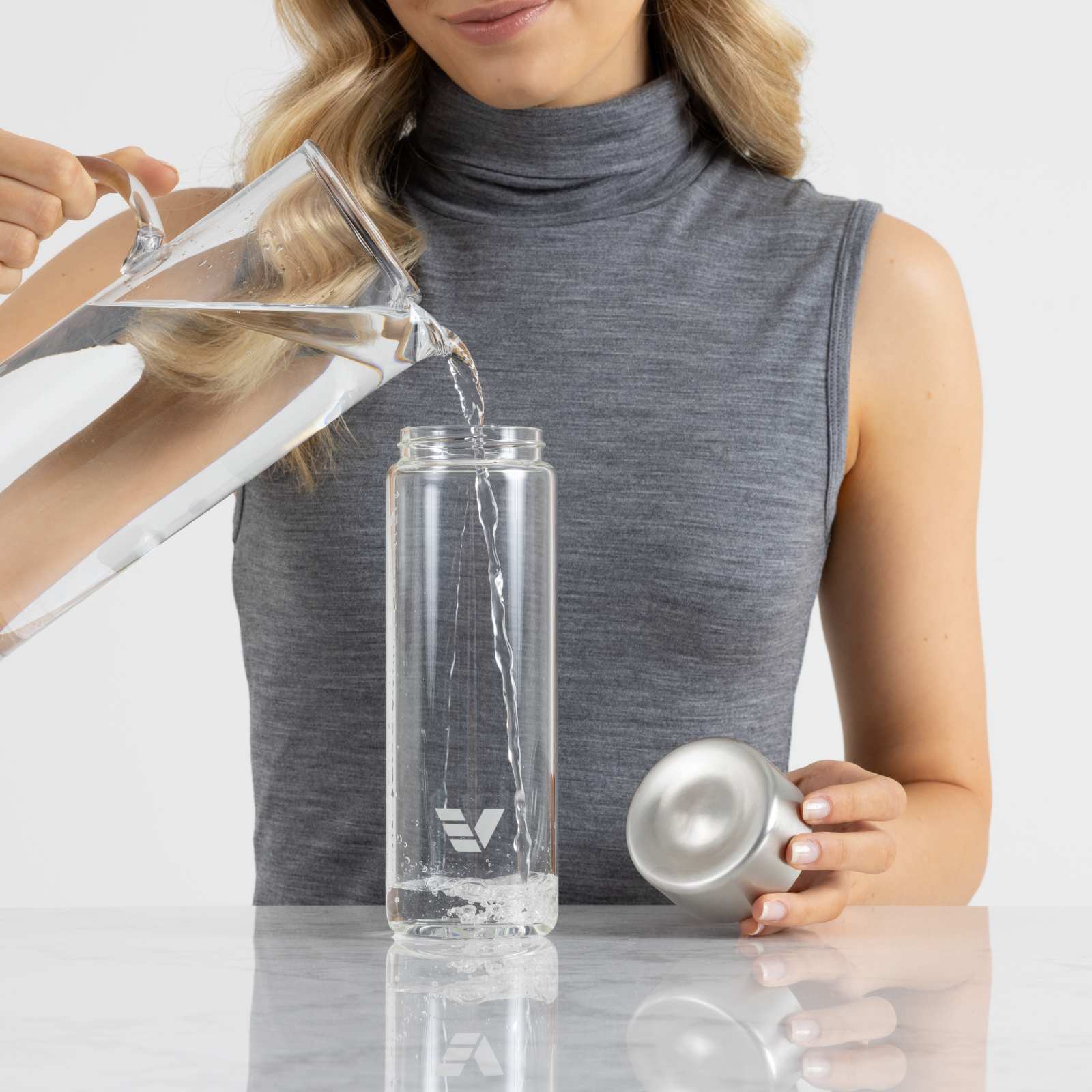 A female filling her Ever Vessel Glass water bottle with stainless steel lid at the kitchen bench.