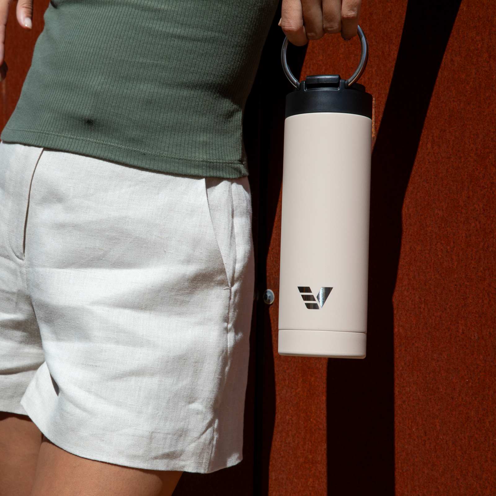 Female holding her Ever Vessel Maxi Desert Beige stainless steel water bottle by the integrated carry handle.