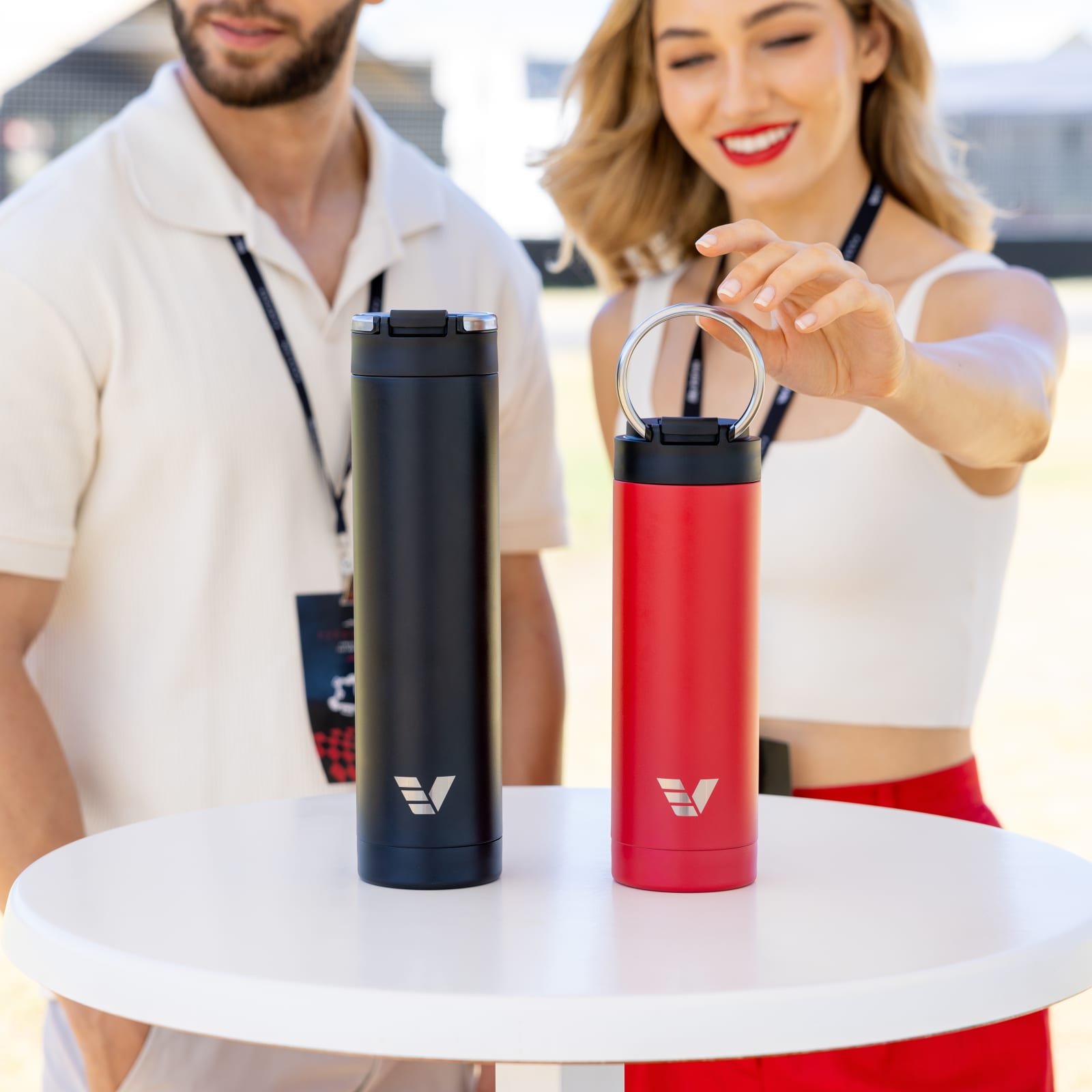 Female and Male attending an event with their Ever Vessel Super Maxi Black and Maxi Red stainless steel water bottles sitting on a round bar table.