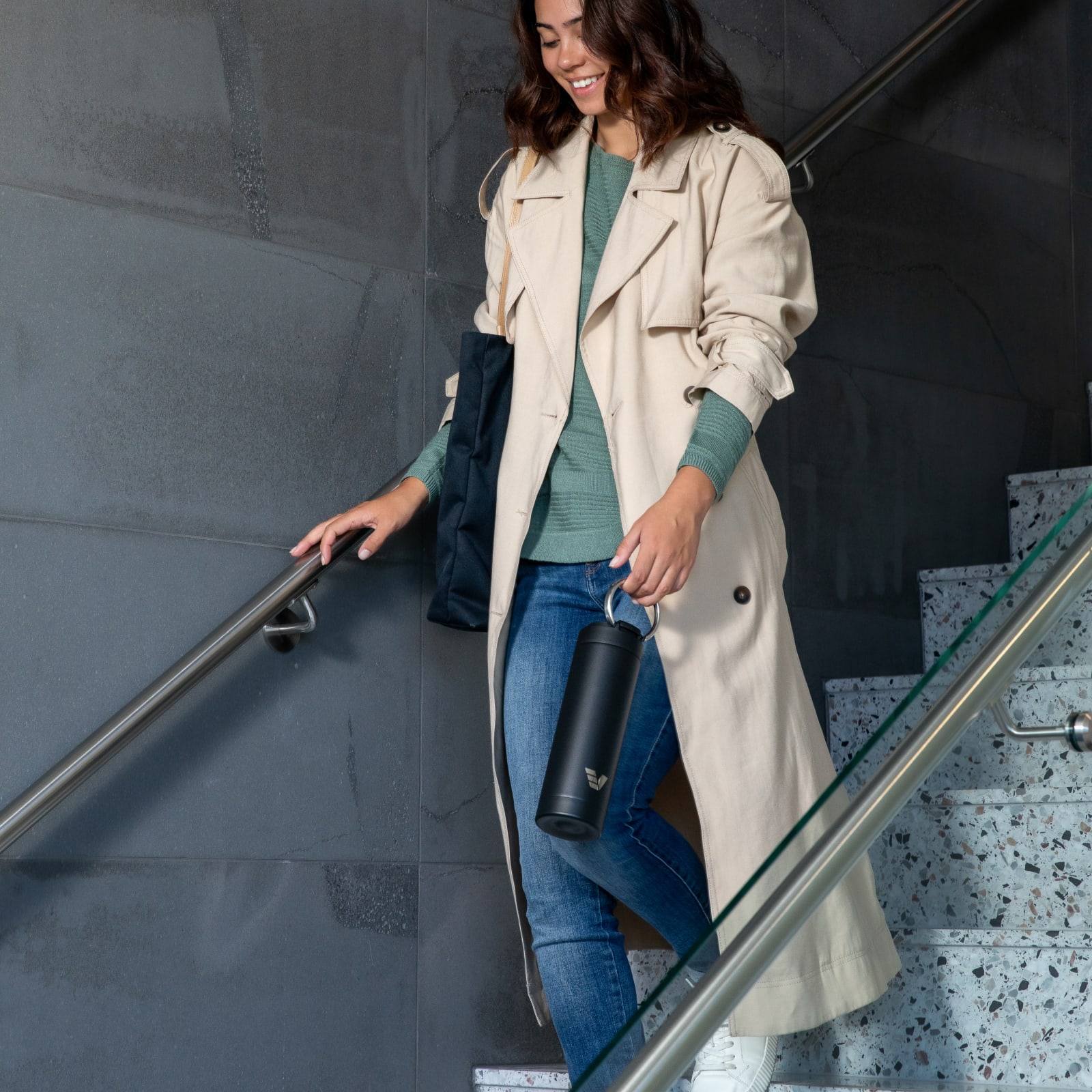 Female walking down the stairs carrying her Ever Vessel Maxi Black stainless steel water bottle by the integrated carry handle.
