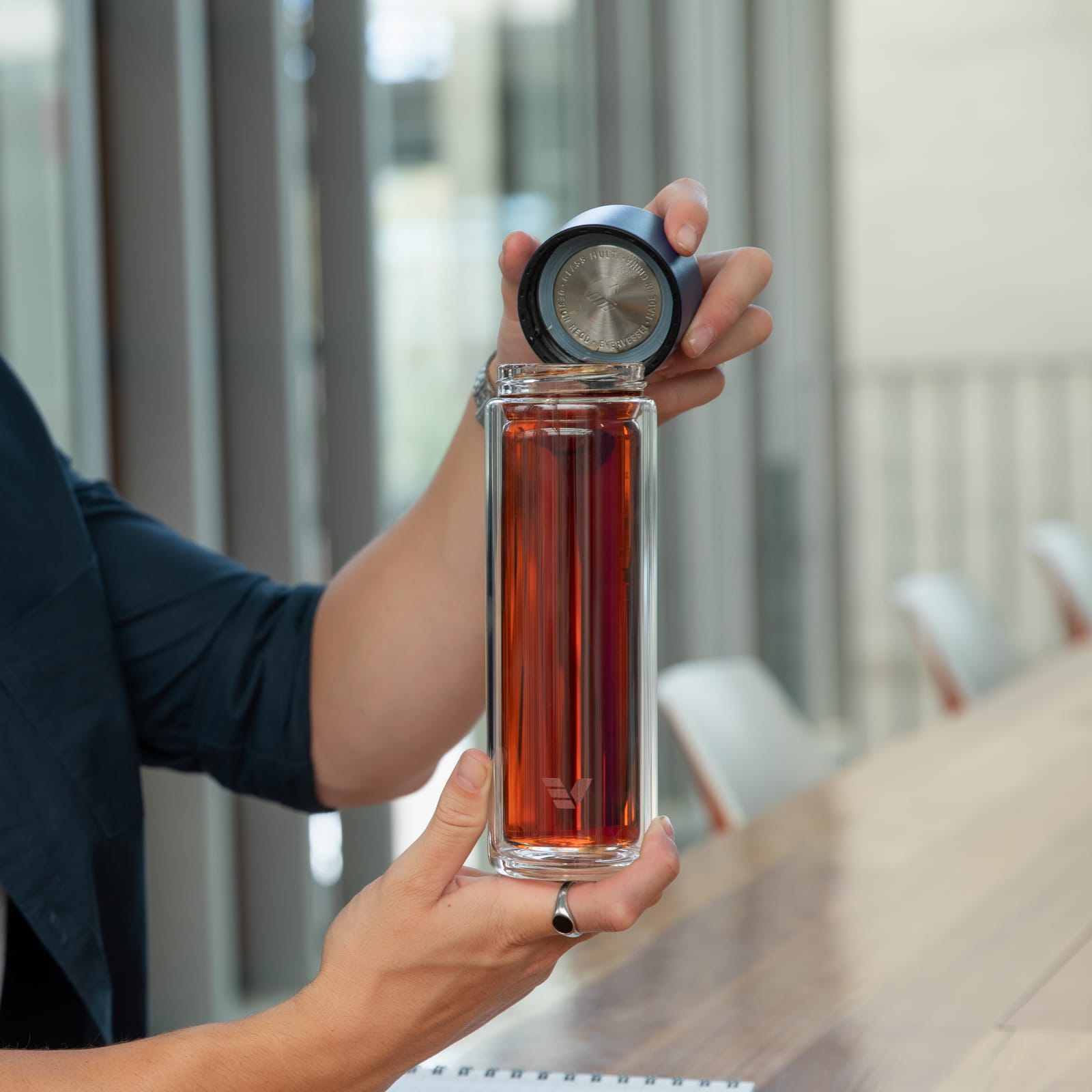 A male taking off the blue lid from his Ever Vessel Glass Multi double wall glass tea infuser water bottle at his desk.