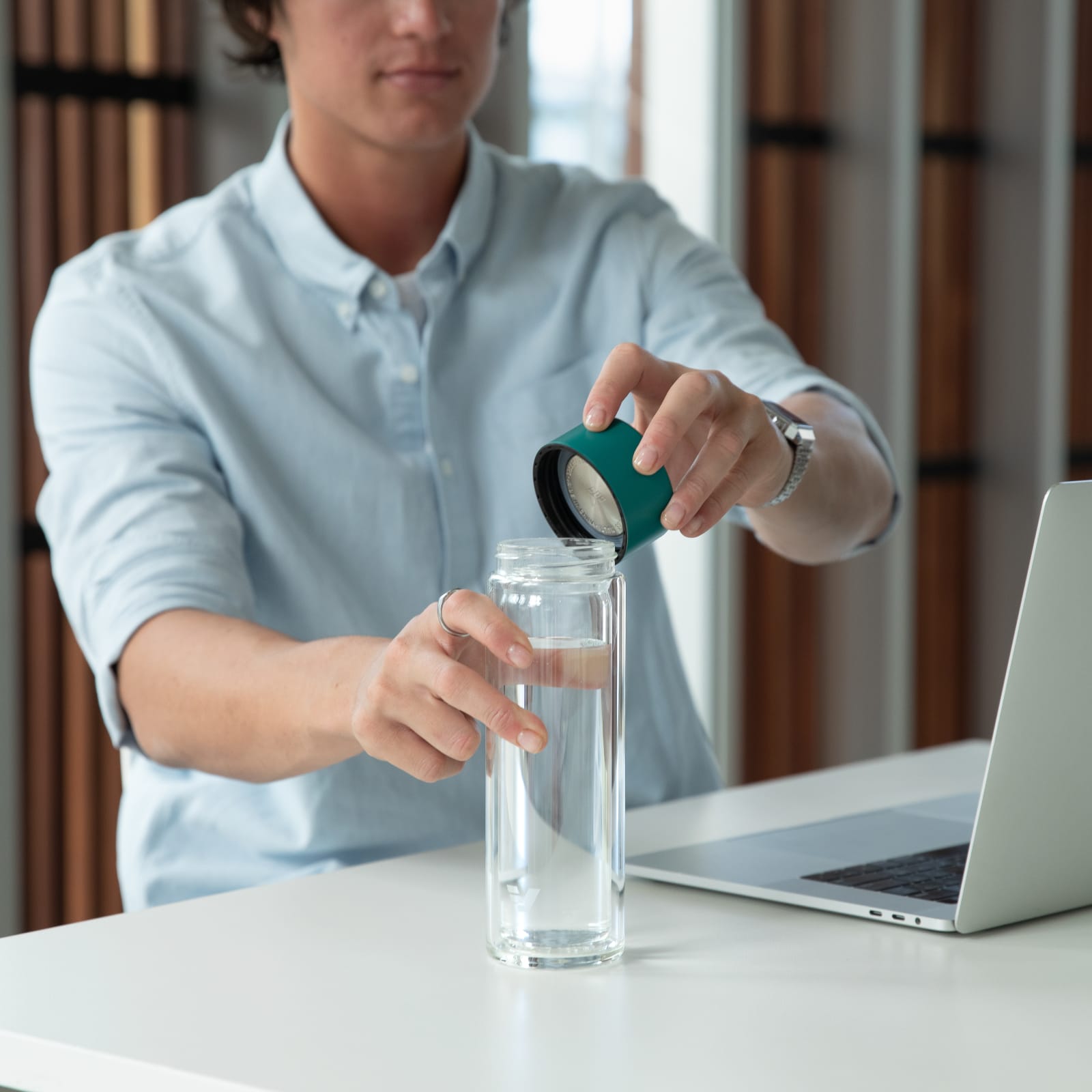 A male taking off the teal green lid from his Ever Vessel Glass Multi double walled glass tea infuser water bottle at his desk.