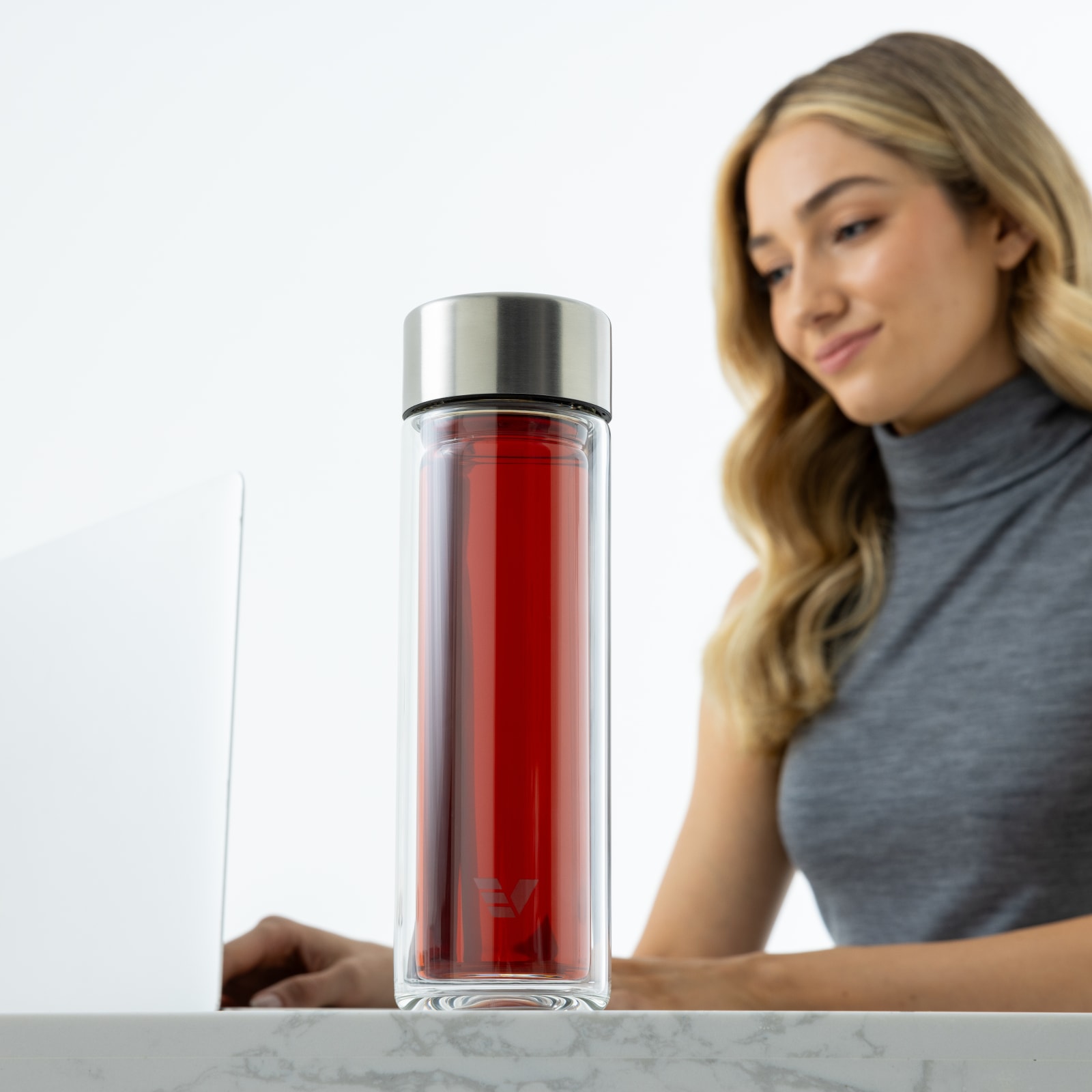 A female at her desk with her Ever Vessel Glass Multi tea infuser water bottle with tea inside by her side.