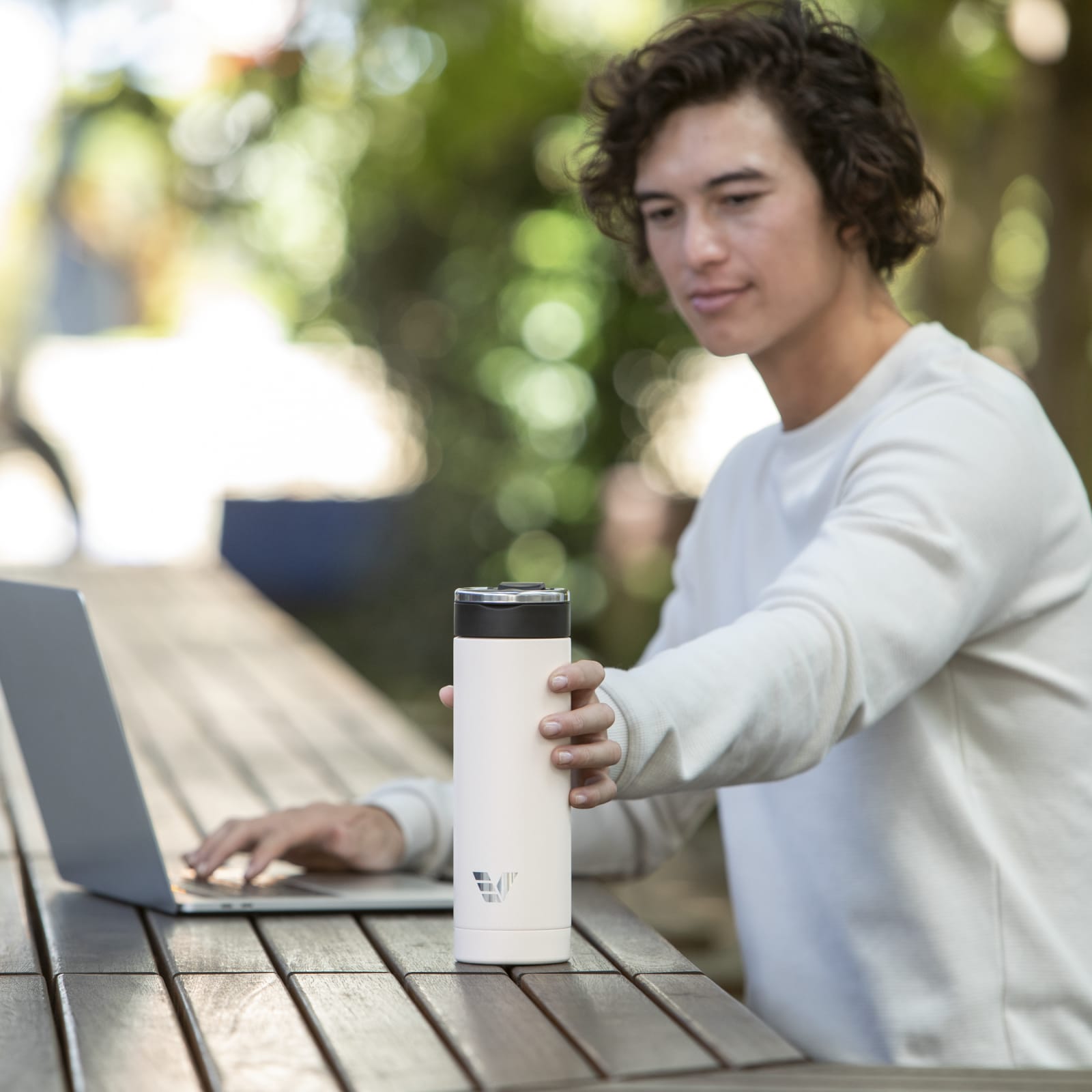 A male reaching for an Ever Vessel Super Maxi stainless steel water bottle in Luna White from an outdoor cafe