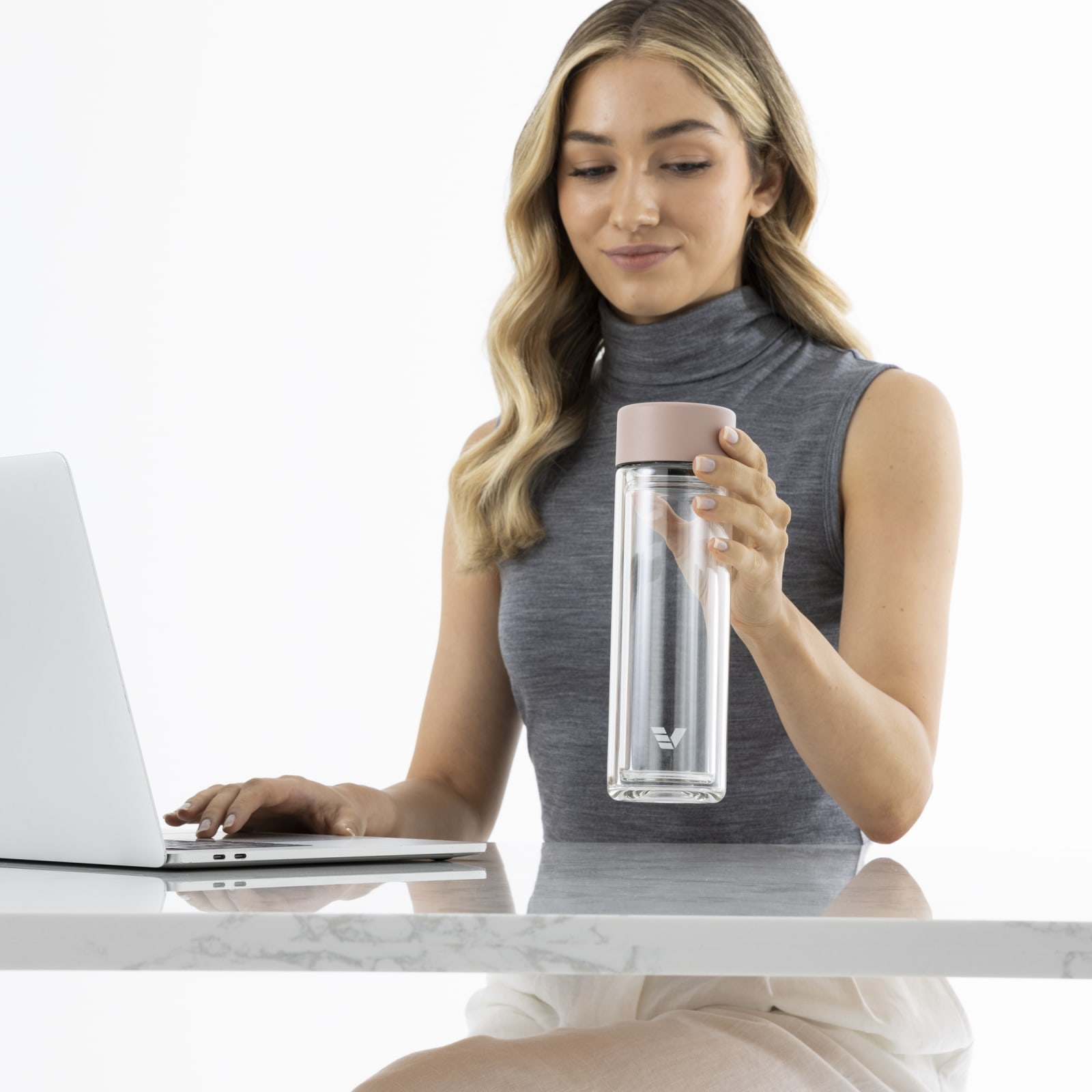 A female holding her Ever Vessel Glass Multi Tea Infuser water bottle above a stone bench at work.