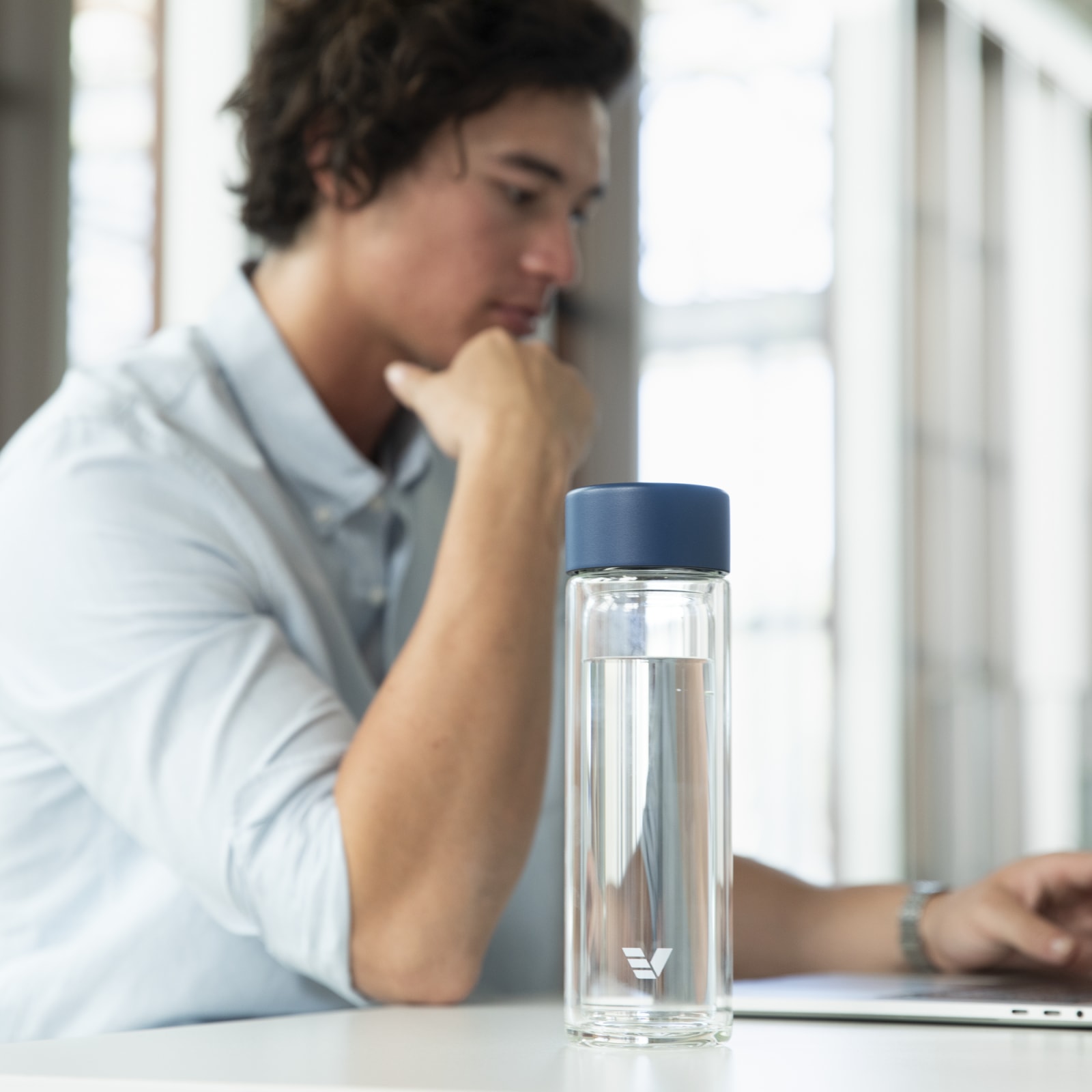 An Ever Vessel Glass Multi tea flask bottle with a teal lid on an office desk.
