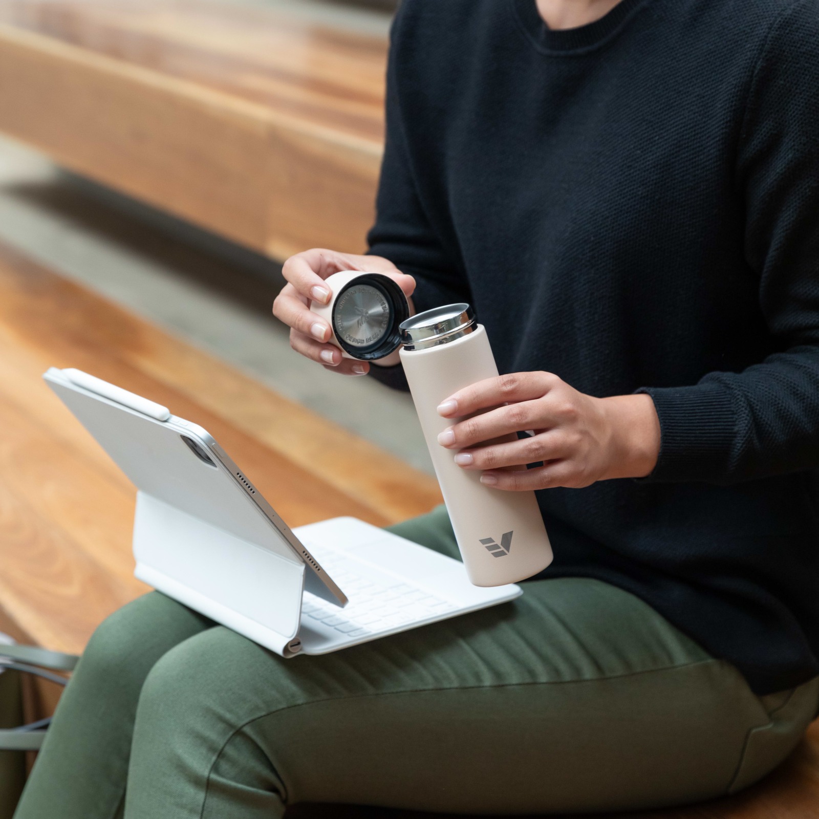 Female about to drink from her Ever Vessel Mini Desert beige small water bottle with lid off.