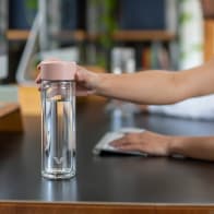 A female reaching for her Ever Vessel Glass Multi Rose Pink double wall tea infuser water bottle from her desk.