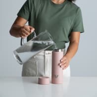 A female filling her Ever Vessel Multi Rose Pink stainless steel tea infuser water bottle with iced water at the kitchen bench.