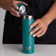 Female taking the lid off her Ever Vessel Mini Teal green small water bottle at a stone bench.