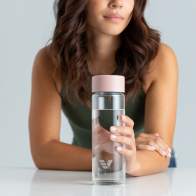 A female holding her Ever Vessel Glass water bottle with rose pink lid on a kitchen bench.