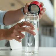 A male taking off the red lid from his Ever Vessel Glass water bottle at his work desk.