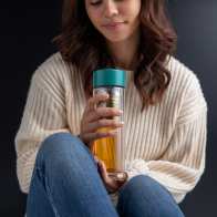 A female holding her Ever Vessel Glass Multi double walled glass tea infuser water bottle with teal green lid and green tea inside.