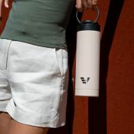 Female holding her Ever Vessel Maxi Desert Beige stainless steel water bottle by the integrated carry handle.