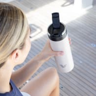 A female about to drink from her Ever Vessel Maxi Desert Beige stainless steel water bottle on a yacht with the leak-proof flip top open.