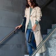 Female walking down the stairs carrying her Ever Vessel Maxi Black stainless steel water bottle by the integrated carry handle.