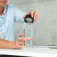 A male taking off the black lid from his Ever Vessel Glass water bottle at his desk.