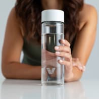 A female holding her Ever Vessel Glass water bottle with white lid above a stone bench.