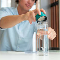 A male taking off the teal green lid from his Ever Vessel Glass water bottle at his desk.