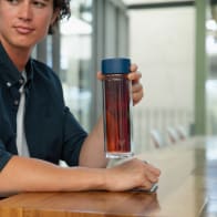 Male holding an Ever Vessel Glass Multi Blue double wall glass tea infuser water bottle with blue lid and tea inside at his desk.