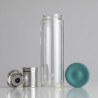 A Glass Multi tea infuser flask bottle sitting on a bench with the tea infuser and lid sitting separately.