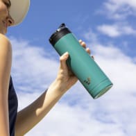 A female about to drink from her Ever Vessel Maxi teal green stainless steel water bottle at the golf course with the leak-proof flip top open.