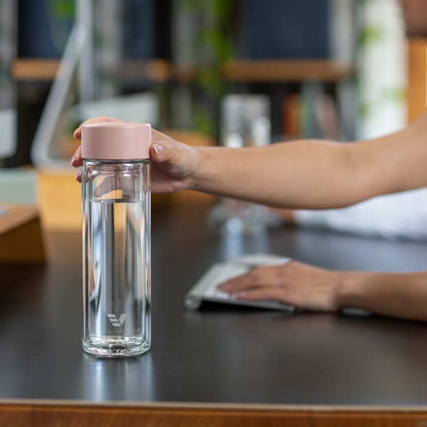 A female reaching for her Ever Vessel Glass Multi Rose Pink double wall tea infuser water bottle from her desk.