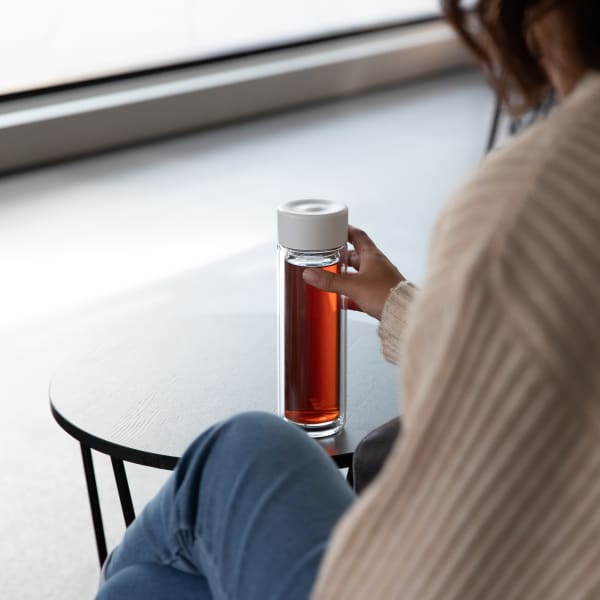 Female holding an Ever Vessel Glass Multi double walled glass tea flask bottle with white colored lid and black infused tea inside.