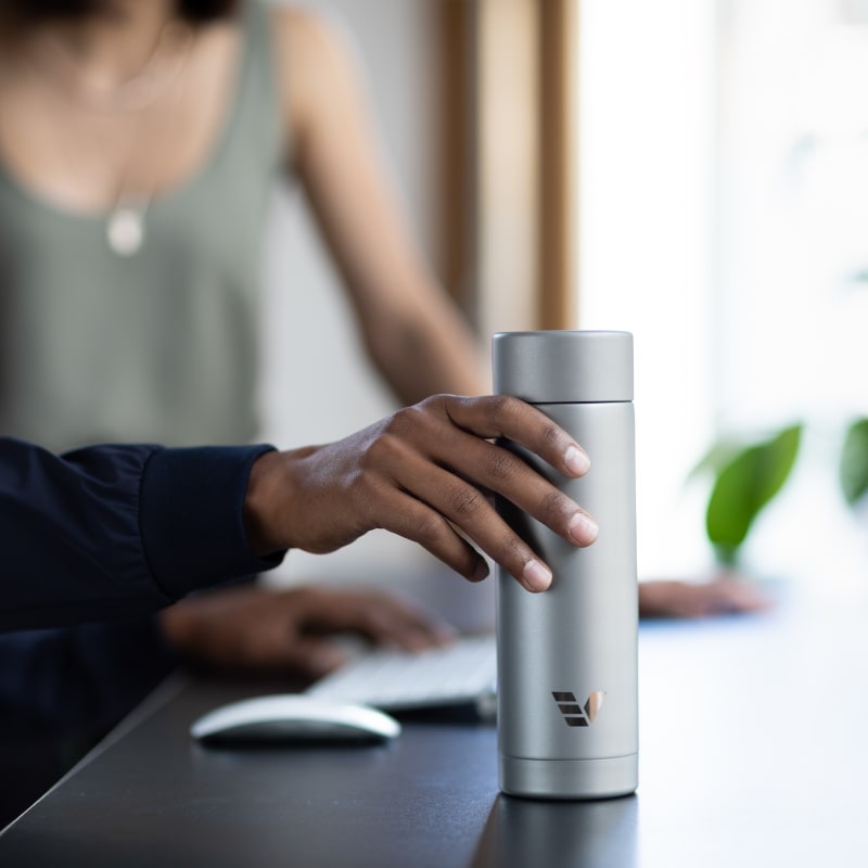 A male picking up his Ever Vessel Multi stainless steel tea infuser water bottle from a desk.