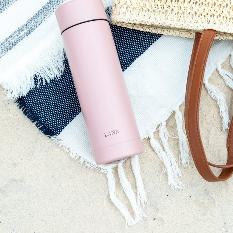 A Personalized Ever Vessel Multi Rose pink stainless steel tea infuser water bottle on a beach towel with the engraved name LANA on the side