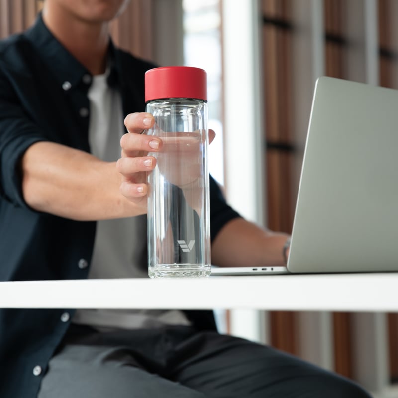 A male reaching for his Ever Vessel Glass Multi double walled tea infuser water bottle with a red lid at a desk