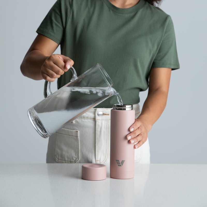 A female filling her Ever Vessel Multi Rose Pink stainless steel tea infuser water bottle with iced water at the kitchen bench.