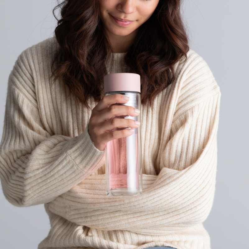 Female holding a Ever Vessel Glass Multi double walled glass tea infuser bottle with the rose pink lid and berry infused tea inside.