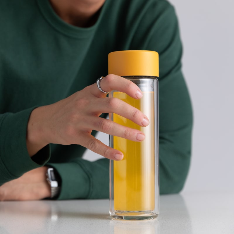 A male holding an Ever Vessel Glass Multi double walled glass tea infuser water bottle with a yellow lid and turmeric tea inside.