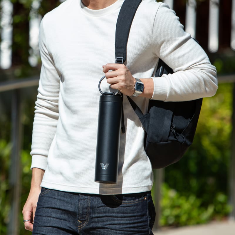A male carrying his Ever Vessel Super Maxi Black stainless steel water bottle by the integrated handle at university.