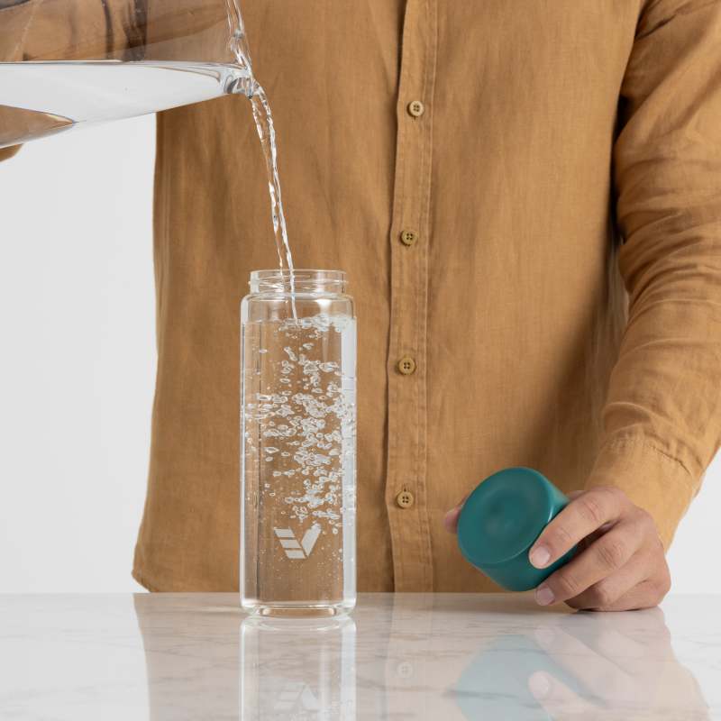 A male filling his Ever Vessel Glass water bottle with teal green lid at the kitchen bench.