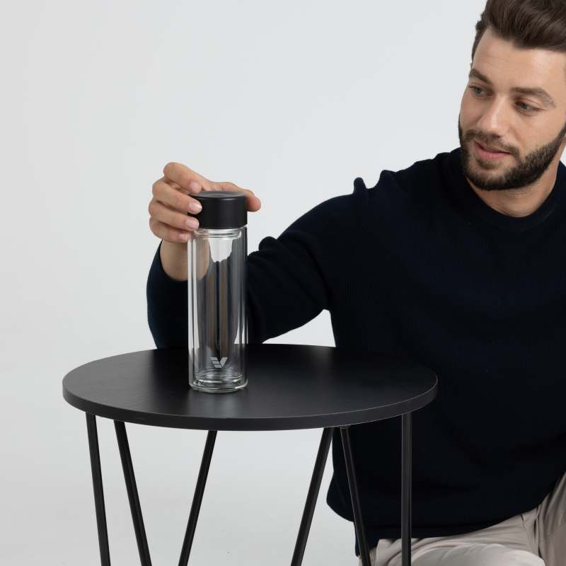 A male picking up his Ever Vessel Glass Multi double walled glass tea infuser water bottle with a black lid off a small side table.
