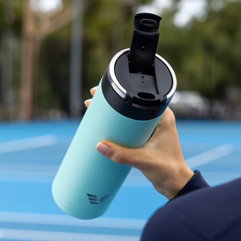 A female about to drink from her Ever Vessel Super Maxi Mint Green stainless steel water bottle with the leak-proof flip top open on the tennis court.