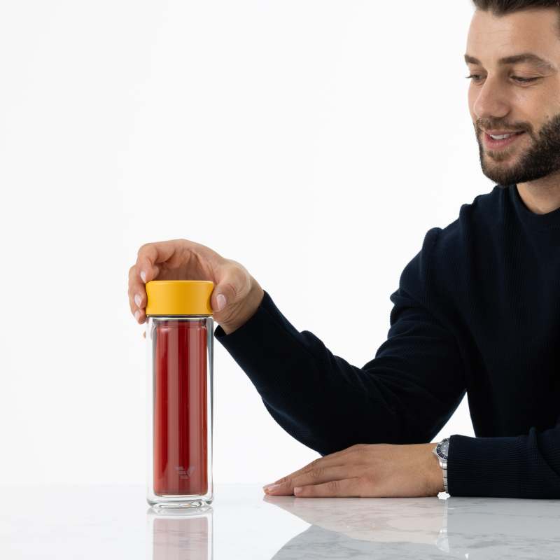 A male lifting an Ever Vessel Glass Multi Yellow double wall glass tea infuser water bottle with black tea inside off his desk.