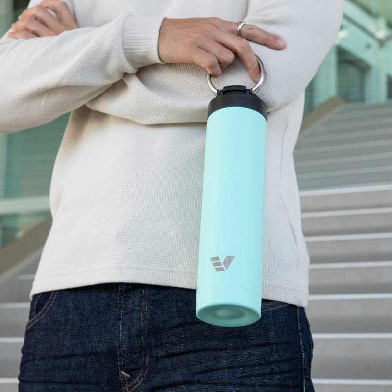 A male holding his Super Maxi Mint stainless steel water bottle by the integrated carry handle on the stairs outside his office.