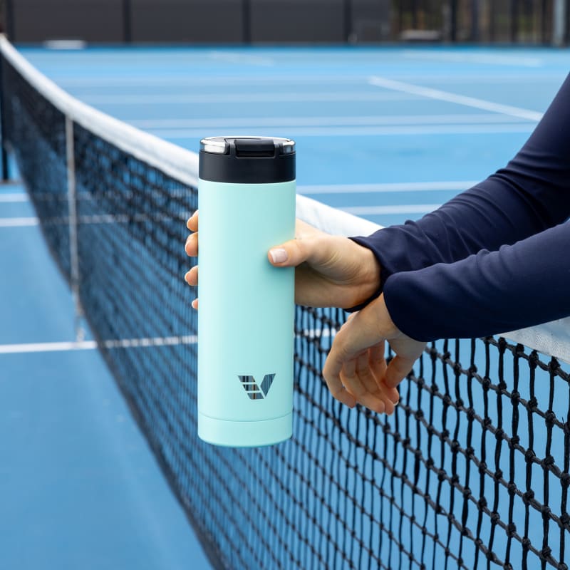 Female holding her Ever Vessel Maxi Mint Green stainless steel water bottle over the tennis court net.