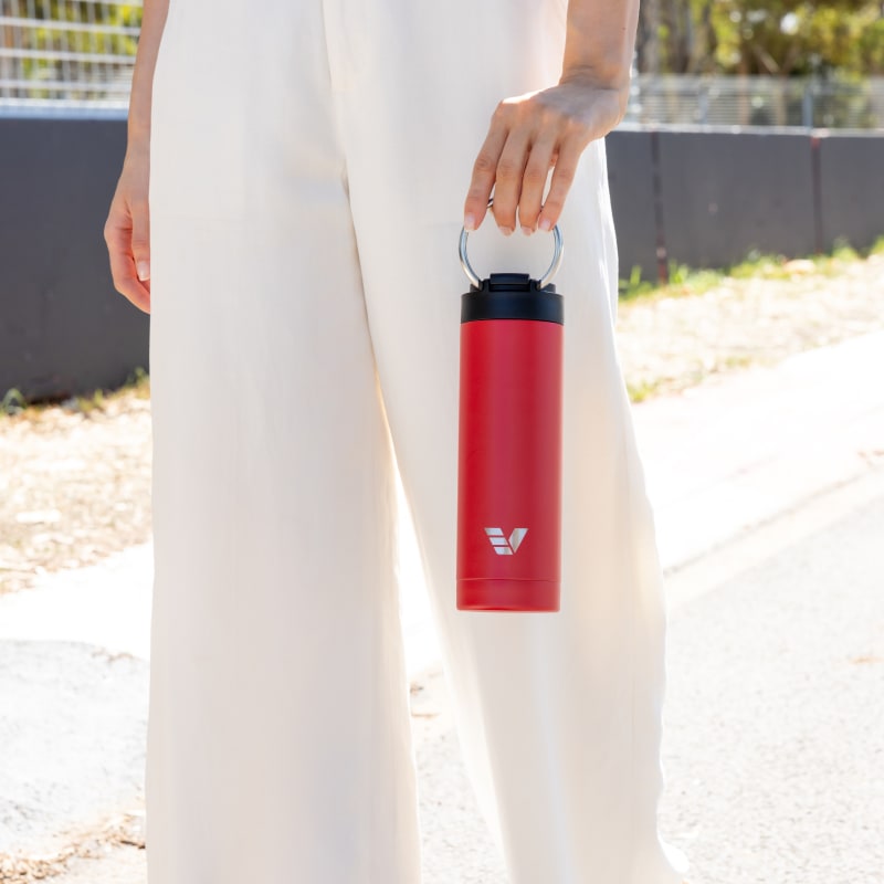 Female carrying her Ever Vessel Maxi Red stainless steel water bottle by the integrated carry handle trackside.