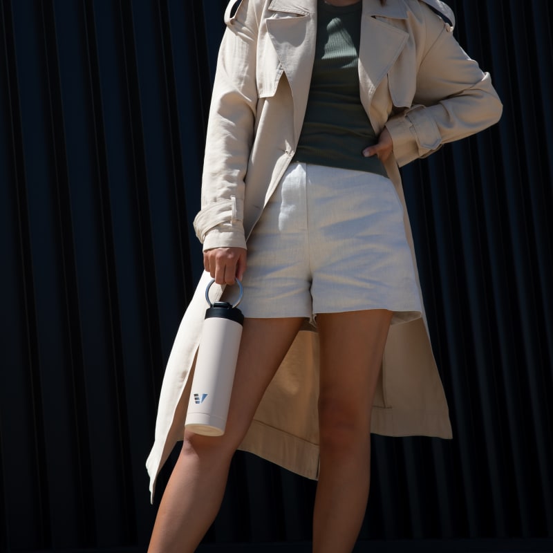Female holding her Ever Vessel Maxi Desert Beige stainless steel water bottle by the integrated carry handle.